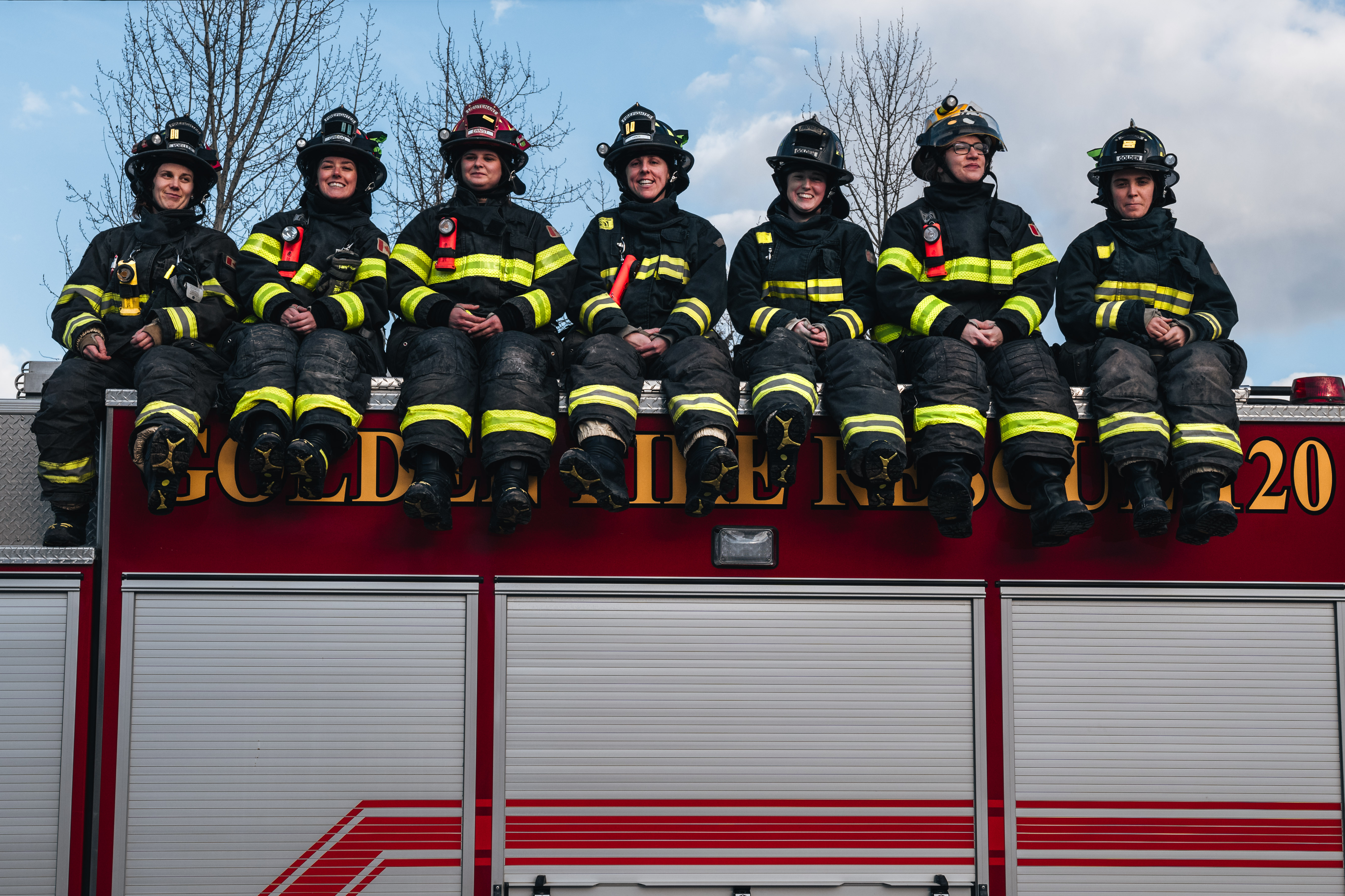 seven female firefighters sitting on top of a fire truck