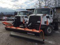 Two snow plows parked in a city works yard